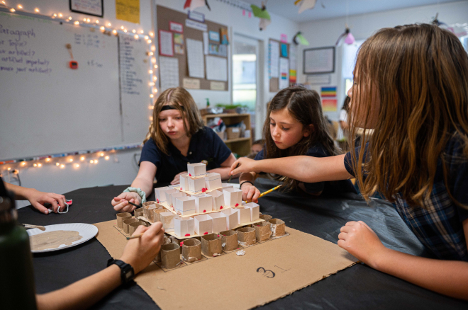 A group of students sitting around a desk concentrating on an activity that teaches about engineering principles.