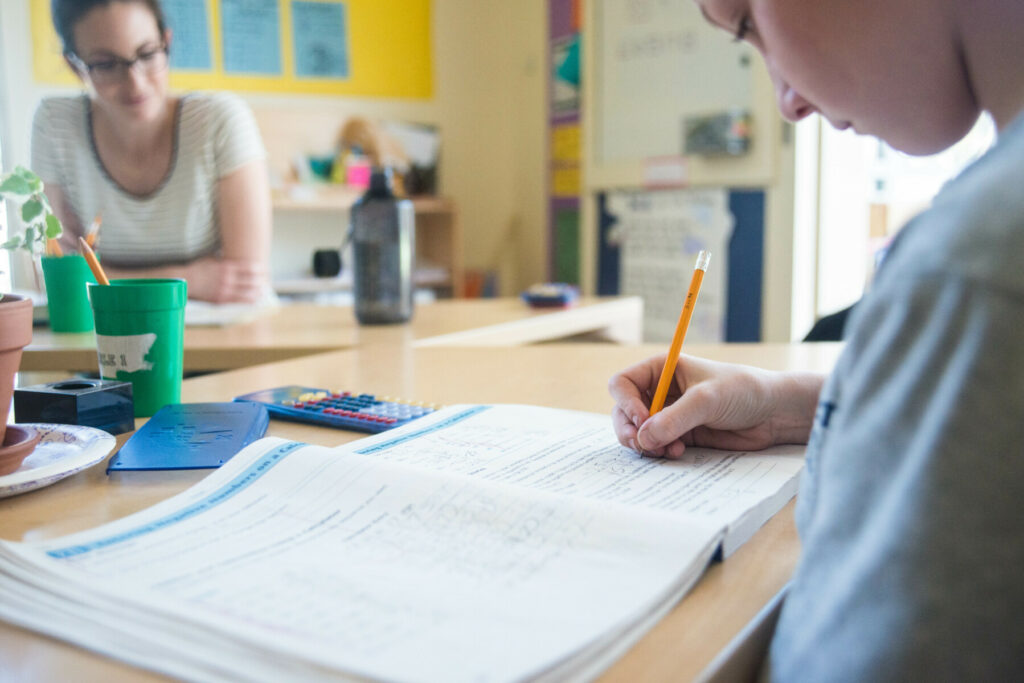 student writing in book alongside teacher