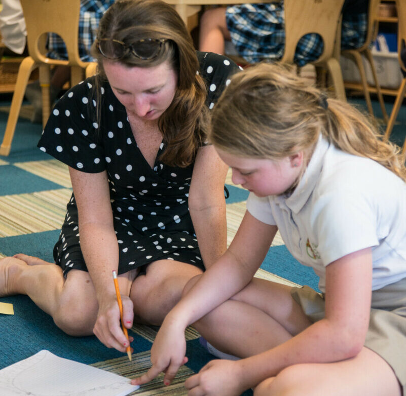 student and teacher sitting on floor looking at paper